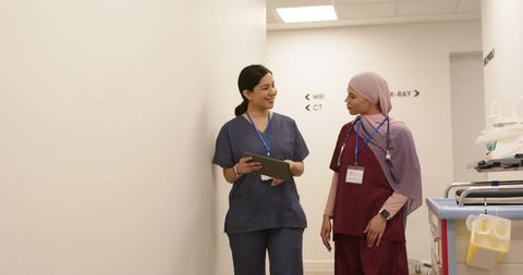 Two female nurses walking hospital corridor consulting tablet and wearing stethoscopes