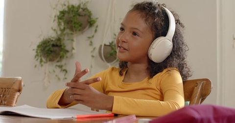 Curly-haired girl studying with white headphones at cozy sunlit table homeschooling