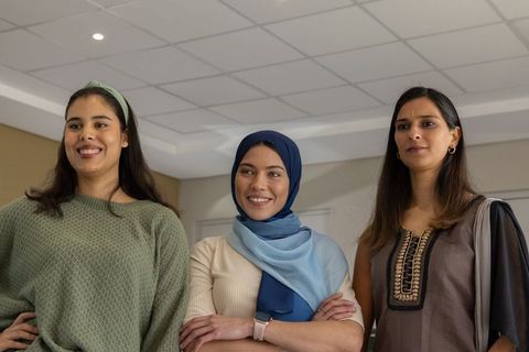 Multicultural women leading in office wearing hijab and smartwatch, confident teamwork