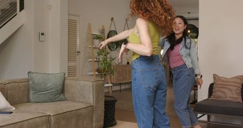 Diverse friends dancing and laughing in cozy living room, casual denim and bright tank