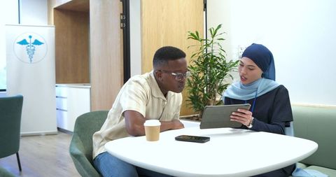 Clinician wearing headscarf consulting patient on tablet in modern clinic
