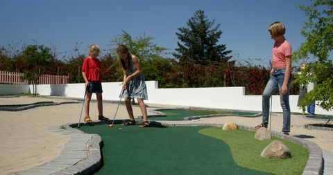 Teen Girls Enjoying Outdoor Mini-Golf Game On Sunny Day