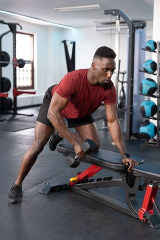 African american man lifting dumbbell and bracing on bench for intense gym training