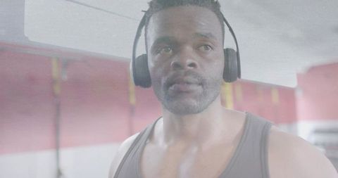 Focused gym training listening to music with over-ear headphones, muscular man concentrating