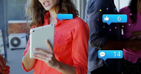 Woman holding tablet reading social media alerts while team collaborating in bright office