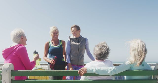 Happy diverse women wearing sports clothes talking at promenade by the sea. Sport, friendship, healthy and active lifestyle.