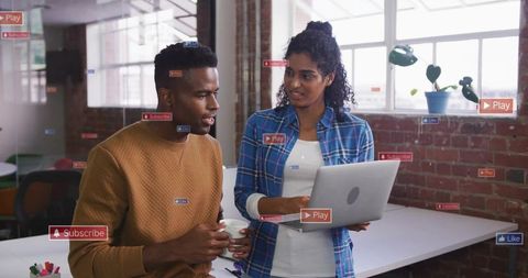 Coworkers collaborating over laptop in industrial office with social media overlays