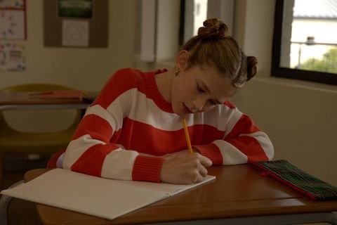 Teen girl writing in notebook at classroom desk wearing red and white striped sweater