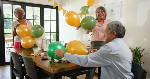 Happy senior friends preparing birthday party with balloons