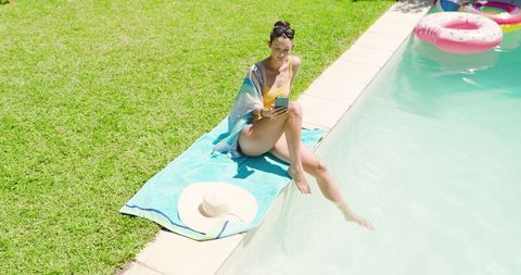 Elegant Woman Relaxing by Poolside with Smartphone