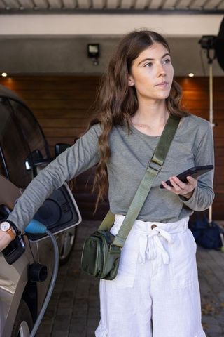 Woman Charging Electric Car in Home Garage Using Smartphone