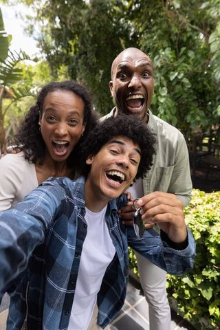 Family celebrating new car keys while taking excited selfie in garden patio