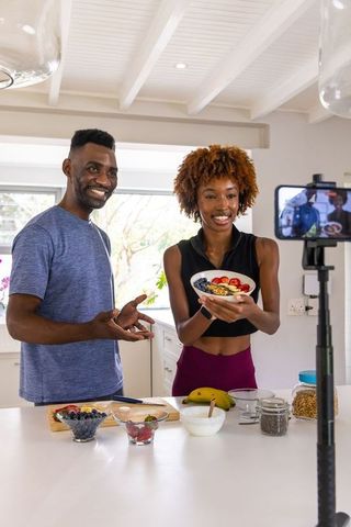 Couple presenting colorful yogurt bowl filming healthy breakfast content in sunlit kitchen