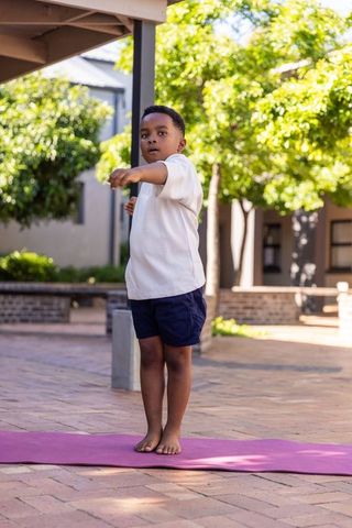 Young african american boy practicing balance on pink yoga mat outdoors on campus
