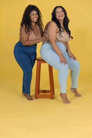 Diverse women laughing together in casual denim and neutral tops on yellow background