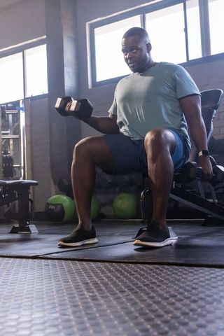 African american man seated dumbbell lifting building strength and focus in gym