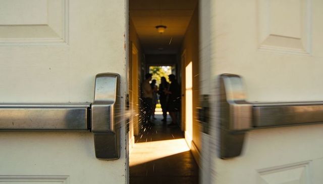 Opening double doors revealing backlit corridor with silhouettes and sunlit particles