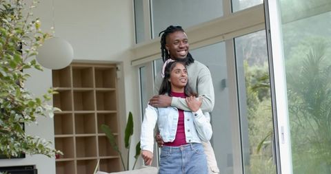 African American man and Indian woman embracing in modern living room with glass doors