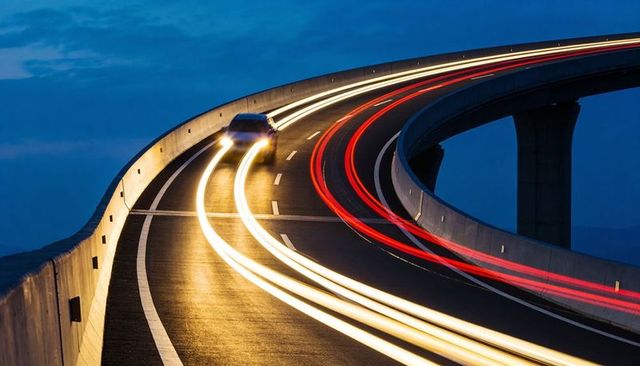 Car carving curved overpass leaving white headlight and red taillight trails at night