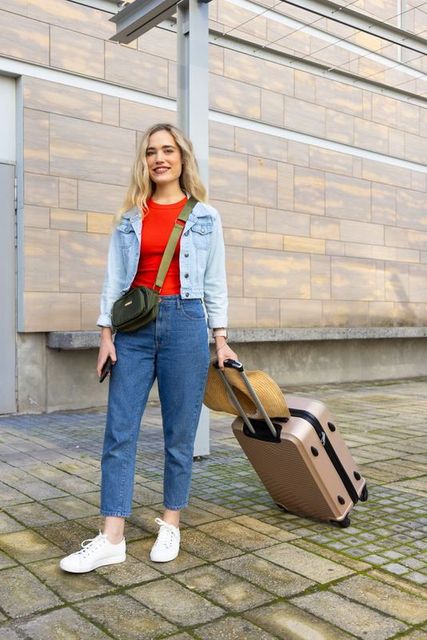 Young woman traveling with rolling suitcase and smartphone on urban plaza streetstyle