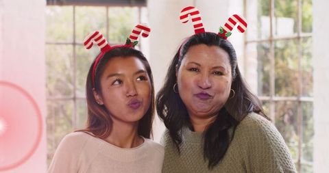Two women wearing candy cane headbands sharing cozy festive family portrait in sunlit home