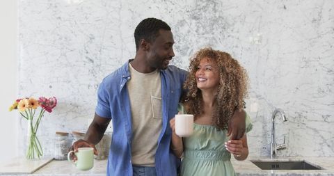 Sharing morning coffee at marble kitchen counter, diverse couple smiling and embracing