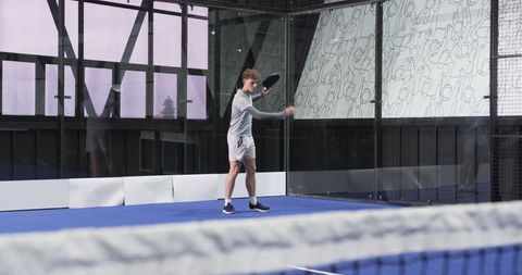 Dynamic padel tennis player in action on glass court