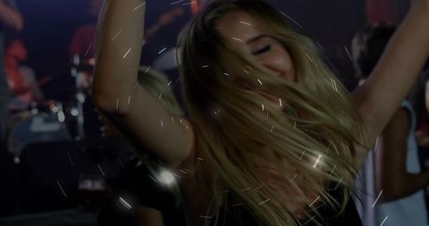 Blonde woman dancing wildly in nightclub with motion blur, stage lights and live band