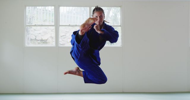 Caucasian female judo fighter in blue kimono kicking at sunny gym. Sport, fitness, health and martial arts, unaltered.