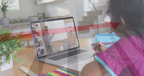 Child learning remotely at home desk taking notes during online lesson with laptop