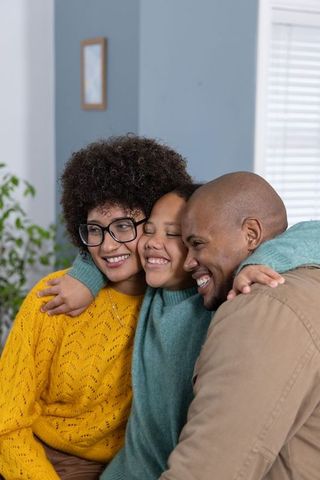Diverse family hugging on sofa sharing cozy embrace and joyful smiles in warm home