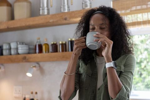 Woman savoring morning coffee in cozy kitchen with wooden shelves and ceramic mug