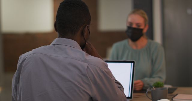 Coworkers using laptops in an office setting, wearing face masks to ensure safety during the pandemic. Ideal for illustrating modern office culture, teamwork, and business meetings in COVID-19 context. Useful for blogs, articles, and presentations on remote work, office protocols, and workplace safety.