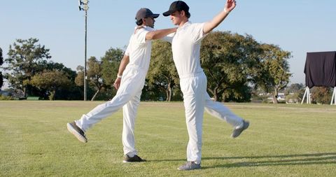Diverse cricket teammates stretching and balancing on outfield during warmup routine