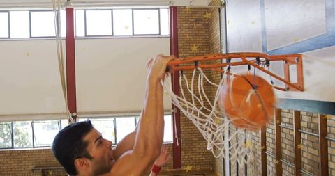 Basketball player dunking and grabbing rim in school gym with motion blur and orange ball