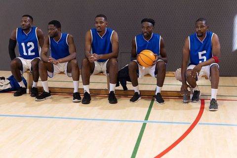 African american basketball players sitting on bench holding basketball awaiting play