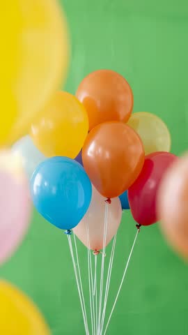 Vertical video of colorful helium balloons floating on green screen with drifting yellow balloon