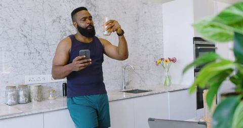 Man checking smartphone holding drink in modern kitchen
