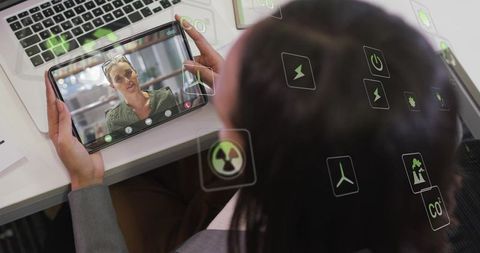 Holding tablet during video call, showing colleague and energy icons for remote collaboration