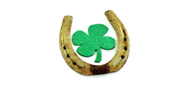 A rusty horseshoe surrounds a green, glittery four-leaf clover against a white background, symbolizing luck and fortune. The combination of the horseshoe and clover is often associated with good luck charms and St. Patrick's Day celebrations.