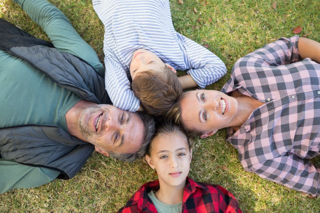 Family lying on grass in park, smiling and enjoying time together. Use for themes of family bonding, outdoor relaxation, happiness, and togetherness in promotional materials, family-oriented content, and advertisements.