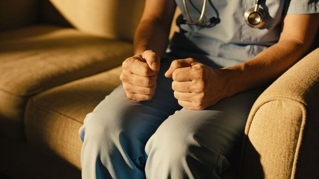 Nurse clenching fists while sitting on sofa in warm light showing stress and fatigue