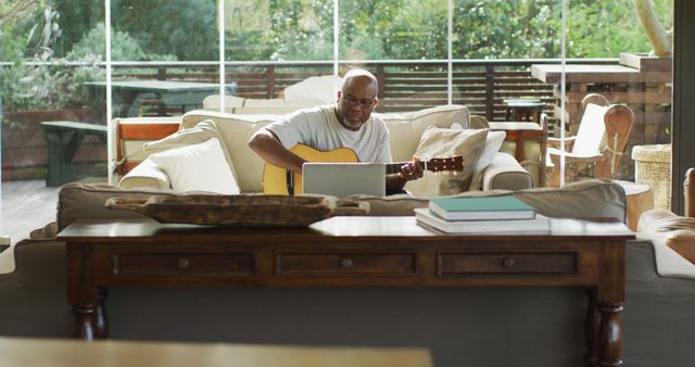 Happy african american senior man in living room playing acoustic guitar and using laptop - Download Free Stock Photos Pikwizard.com
