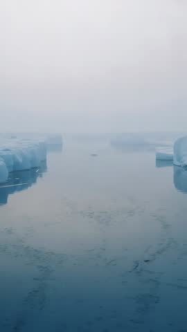 Vertical slow-motion glacial channel with mist drifting over ice floes in polar calm