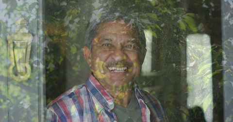 Smiling senior man standing behind glass door with leaf reflections and brass knocker