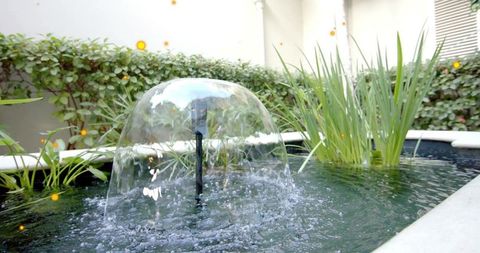 Water dome forming over courtyard pond fountain nozzle with glassy reflections and ripples