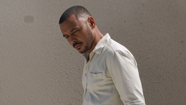 Contemplating man standing by textured concrete wall in sunlit urban casual button-up
