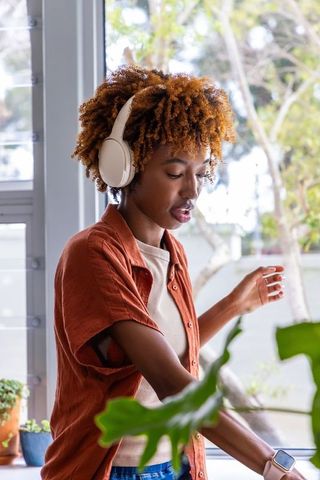 Listening to music while tending indoor plants near sunlit window wearing headphones