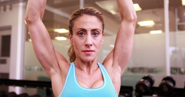 Woman lifting weights at gym, showing determination and strength. Useful for promoting fitness and healthy lifestyle programs, gym advertisements, and motivational posters. Ideal for conveying themes of empowerment and physical fitness.