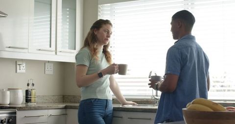 Diverse couple chatting over coffee at kitchen sink with granite countertop